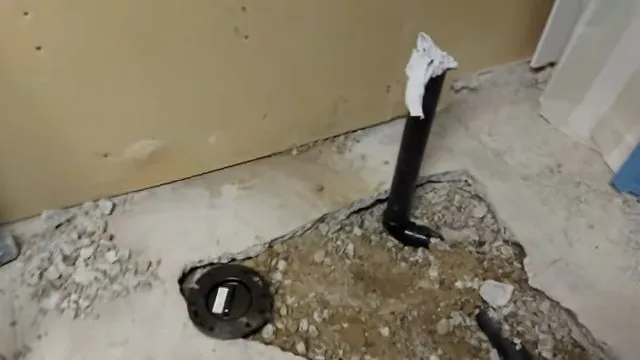 Black pipe standing up through broken concrete where a section of slab has been opened