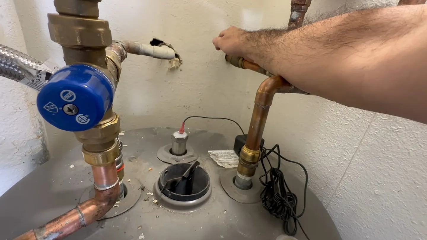 Arm reaching to copper supply lines and a blue-handled valve on top of a tank water heater