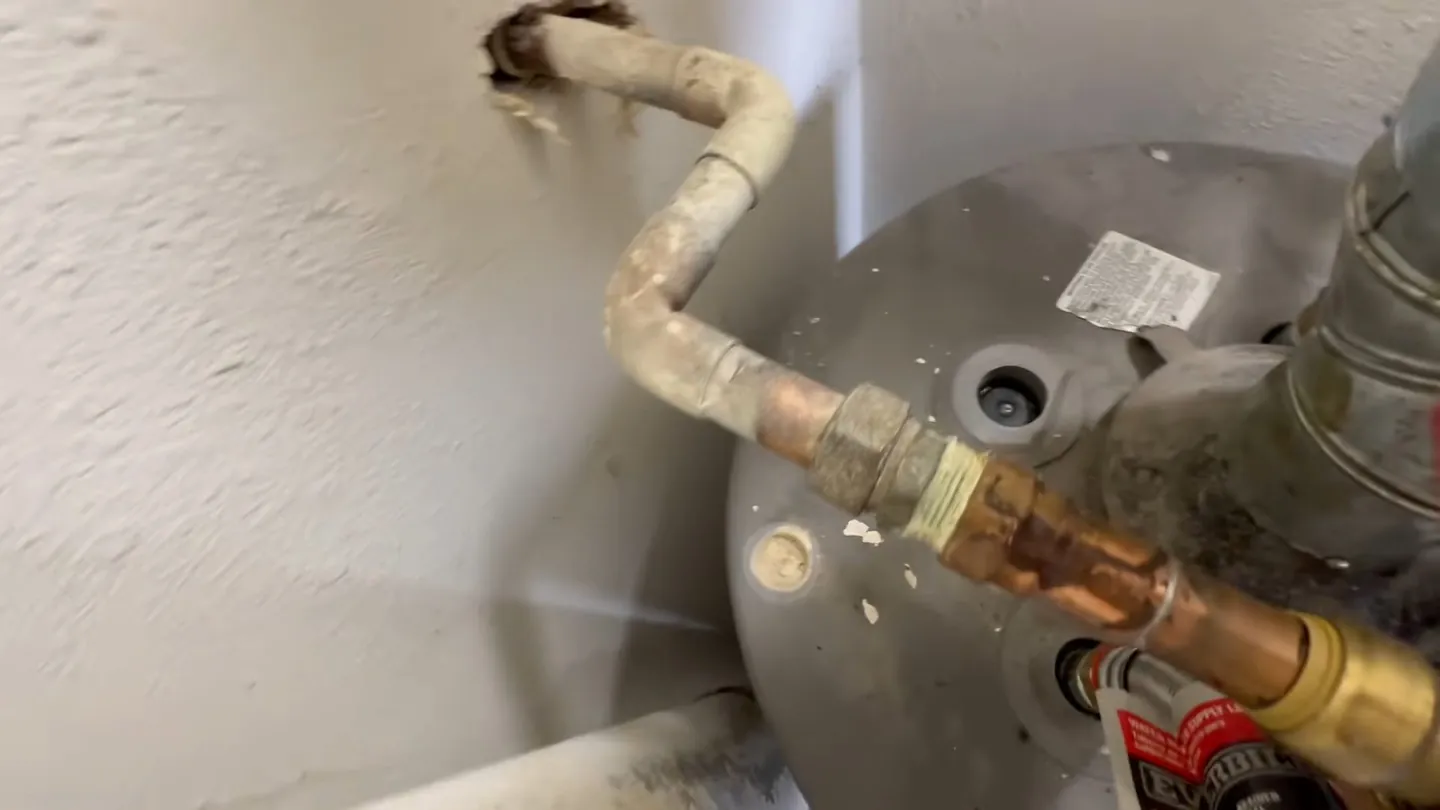 Copper supply pipe with a wrapped fitting running to the top of a gray tank water heater
