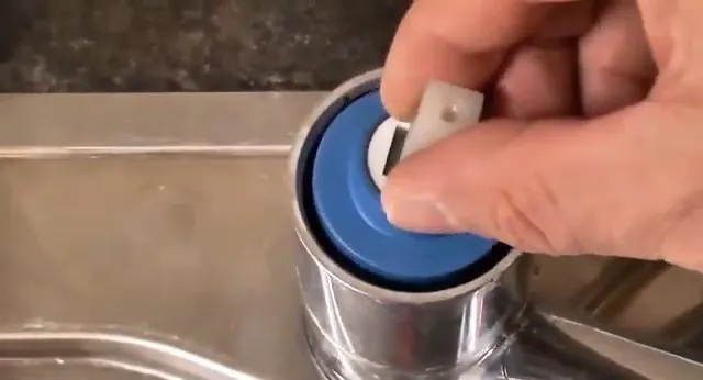 Fingers lifting a blue cartridge cap from the top of a chrome faucet body