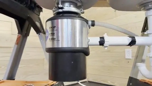 Stainless garbage disposal hanging below a sink with a black drain elbow and a white discharge pipe