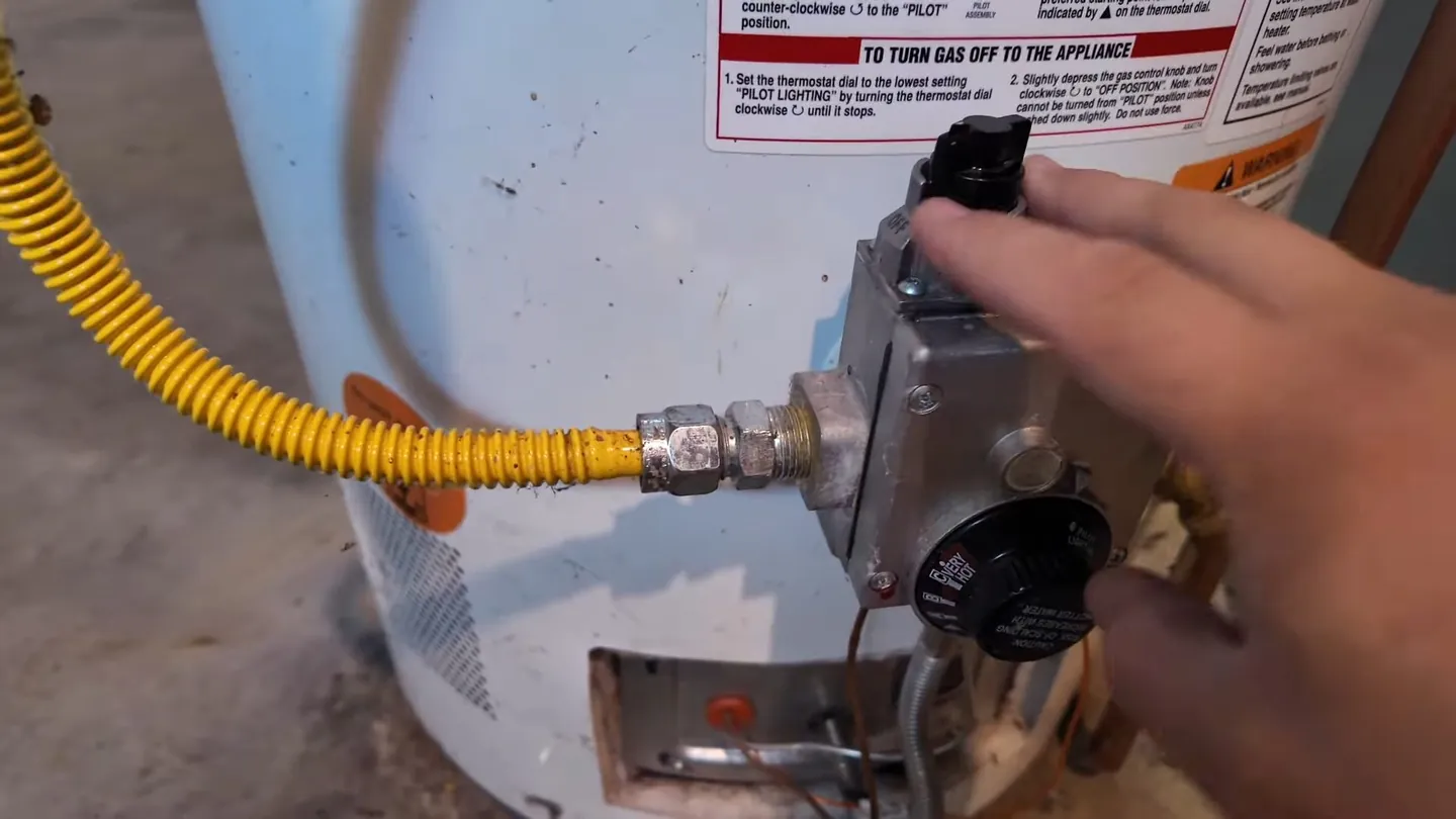 Hand at the gas control valve of a tank water heater with a yellow flexible gas line attached