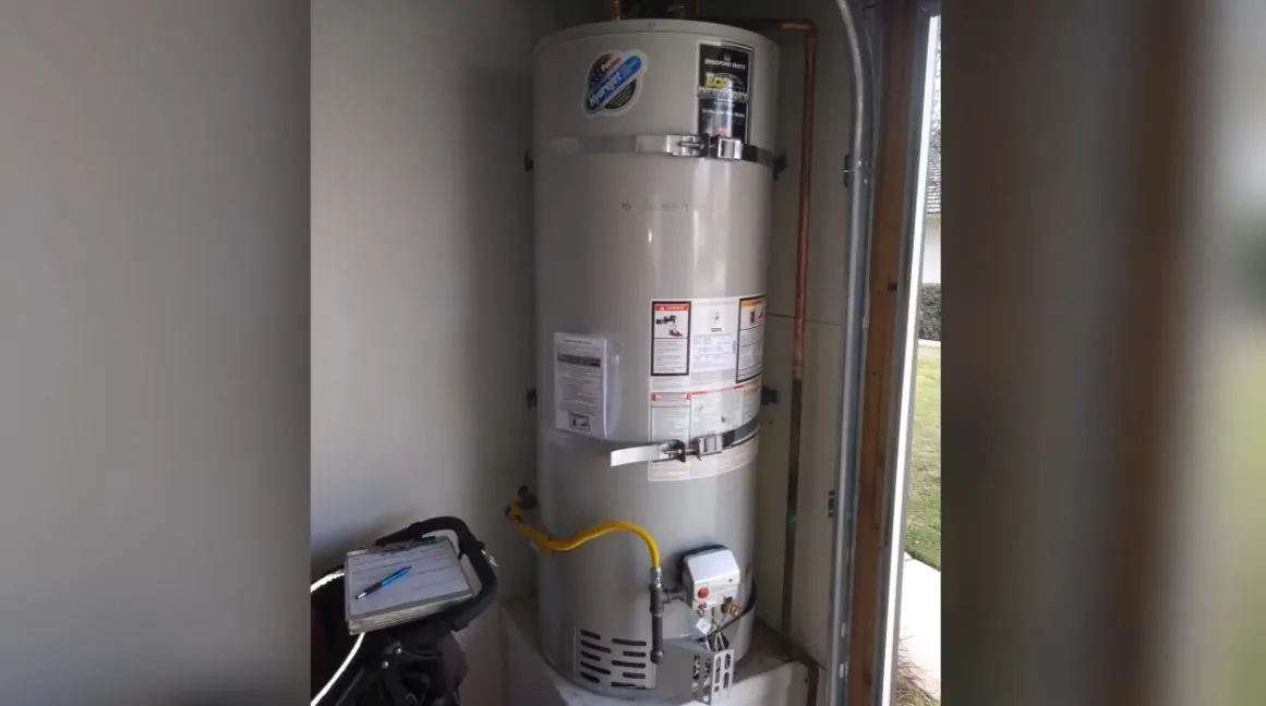 Gas tank water heater standing in a narrow closet with a small box at its base