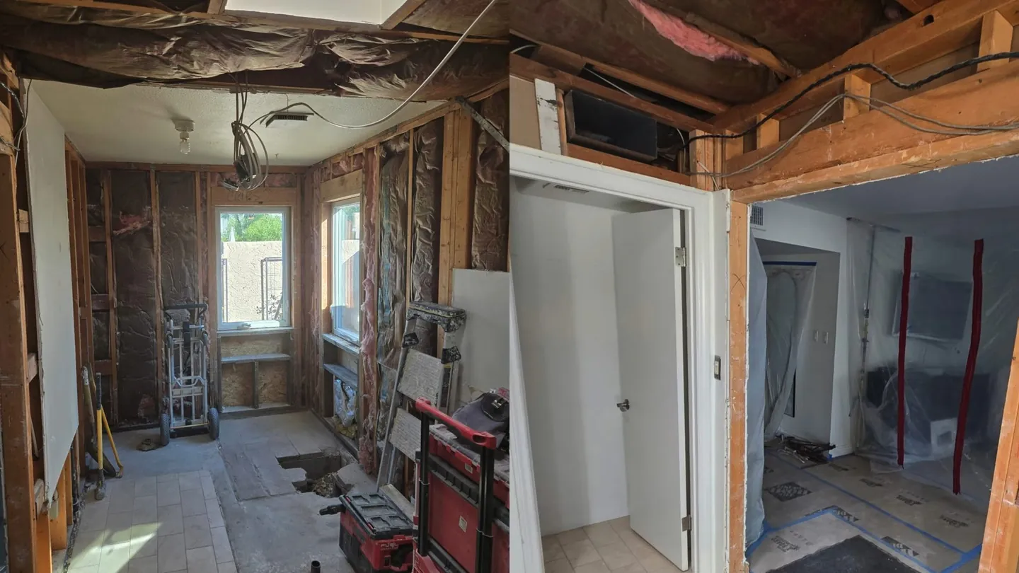 Gutted bathroom and hallway with open studs, hanging wiring and a hand truck, with tile already down on the floor