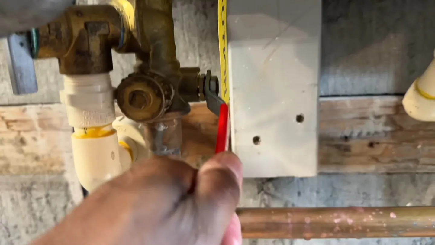 Hand holding a tape measure beside copper pipes and fittings at a water heater connection