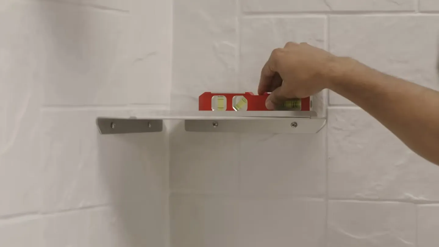Hand placing a small red level on a metal bracket against a white tiled wall