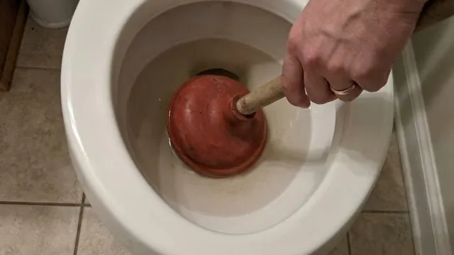 Hand working a red rubber plunger in a toilet bowl