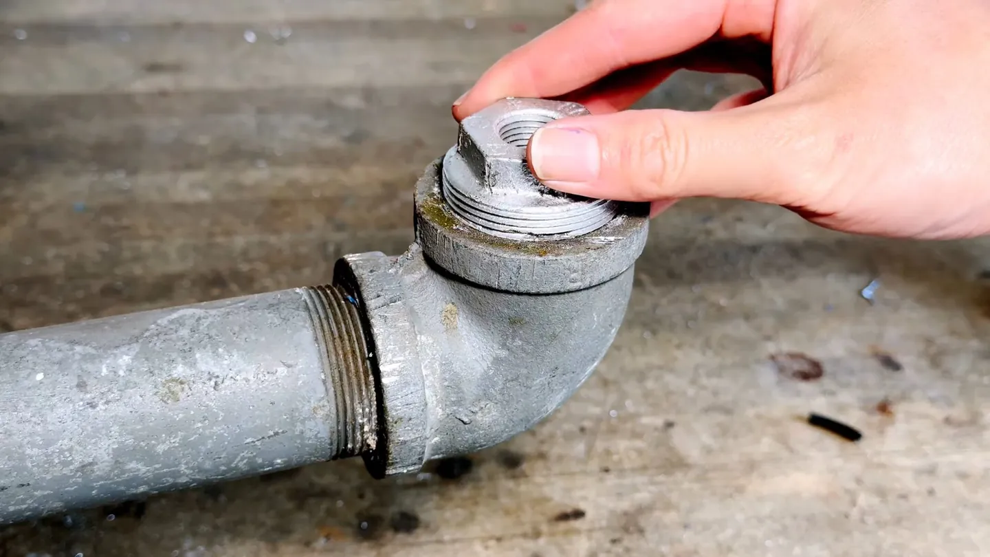 Hand unscrewing the threaded cap from the cleanout of a galvanized pipe elbow