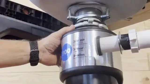 Hand steadying a stainless garbage disposal beneath a sink with a white drain pipe attached