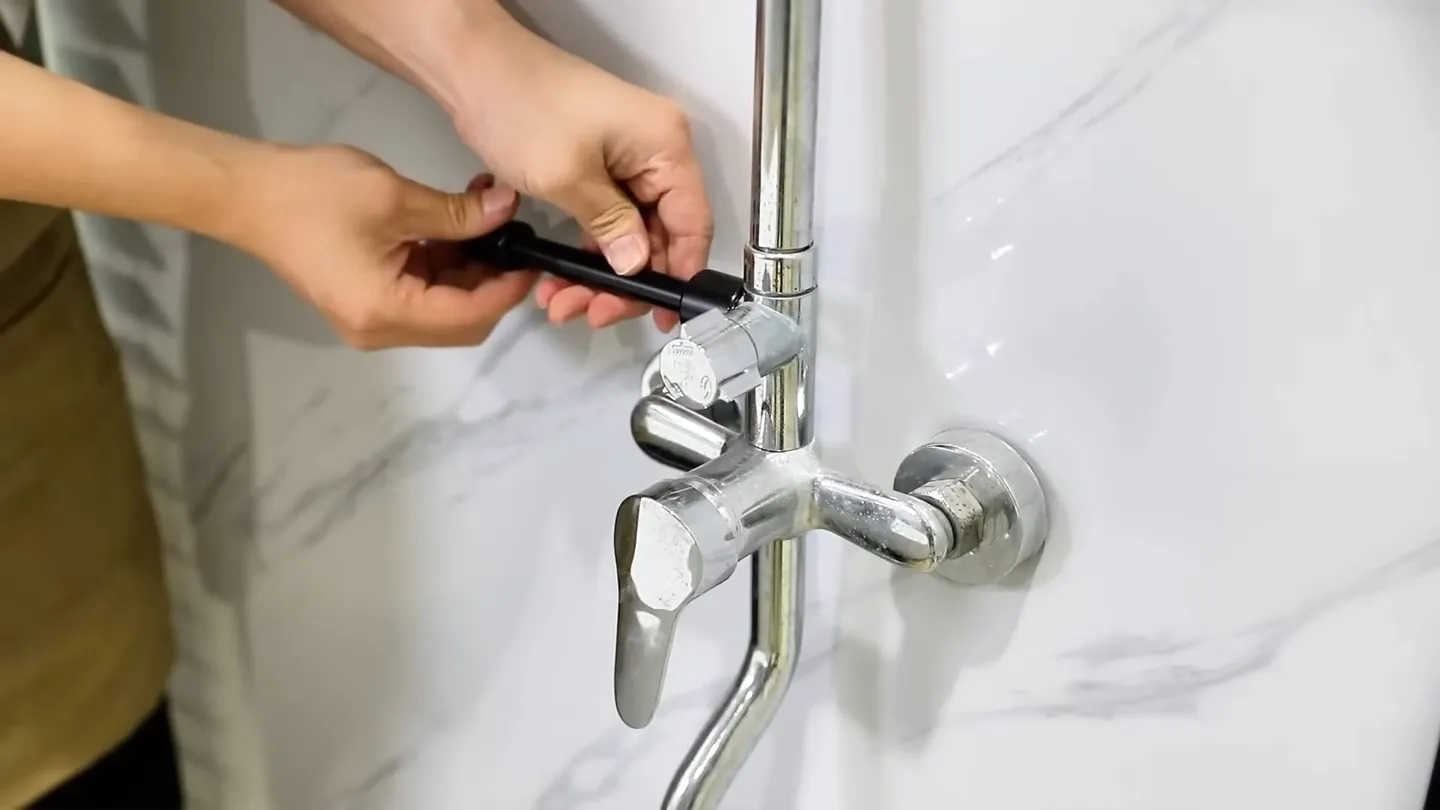 Hand holding a small tool at a chrome shower mixer valve on a marble-look wall