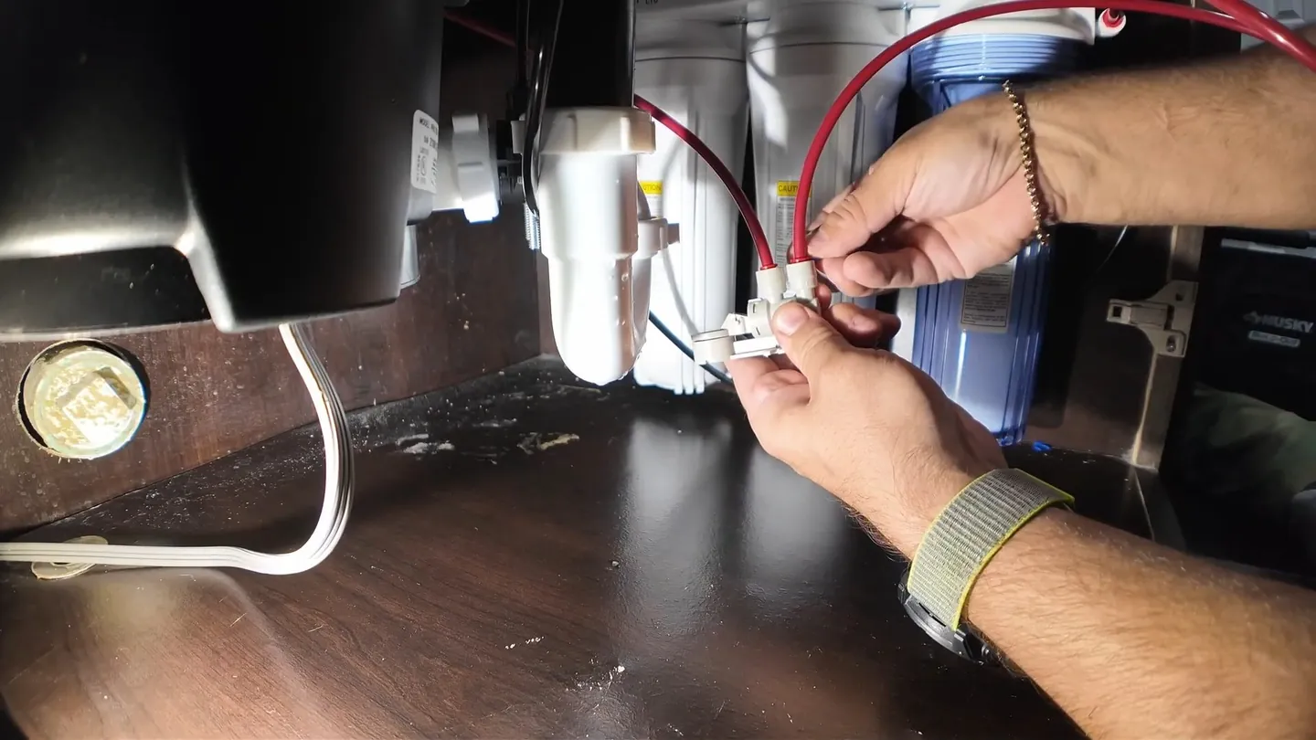Hands connecting tubing and fittings to a small filter unit beneath a countertop