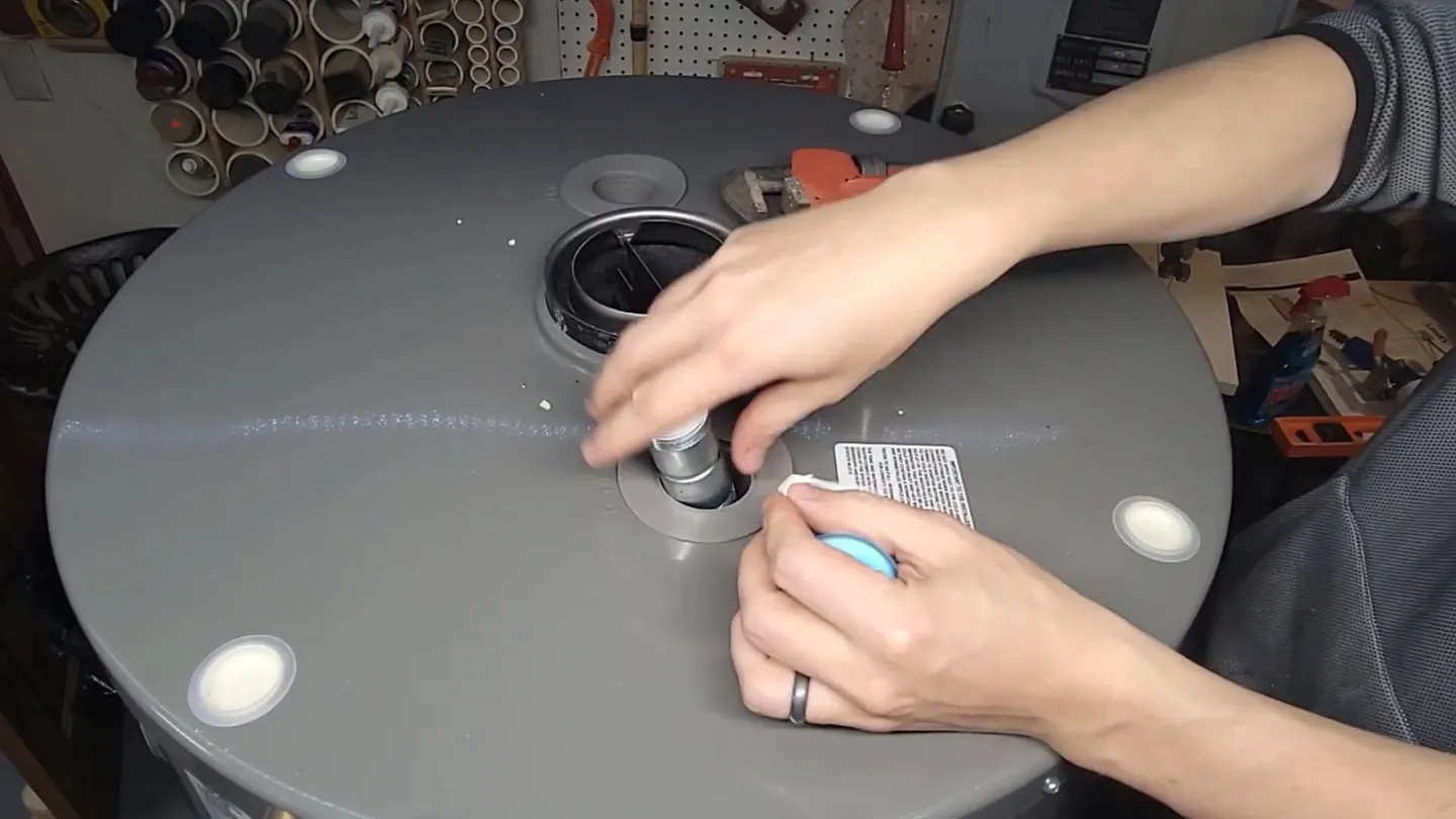 Hands tightening a threaded fitting at the center of a tank water heater's top