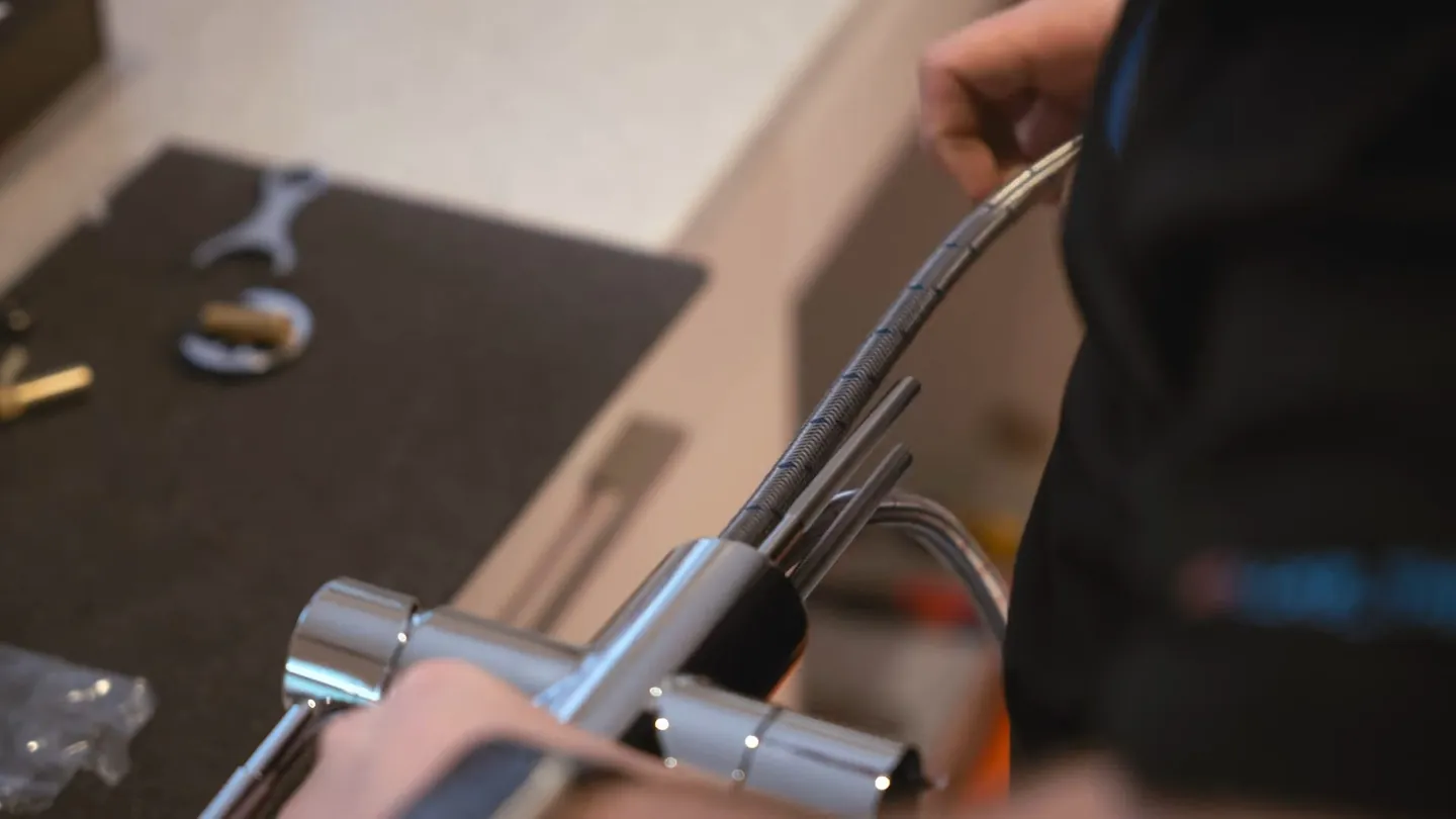 Kitchen faucet with a braided supply hose being fitted, wrench and small parts resting on a dark work mat