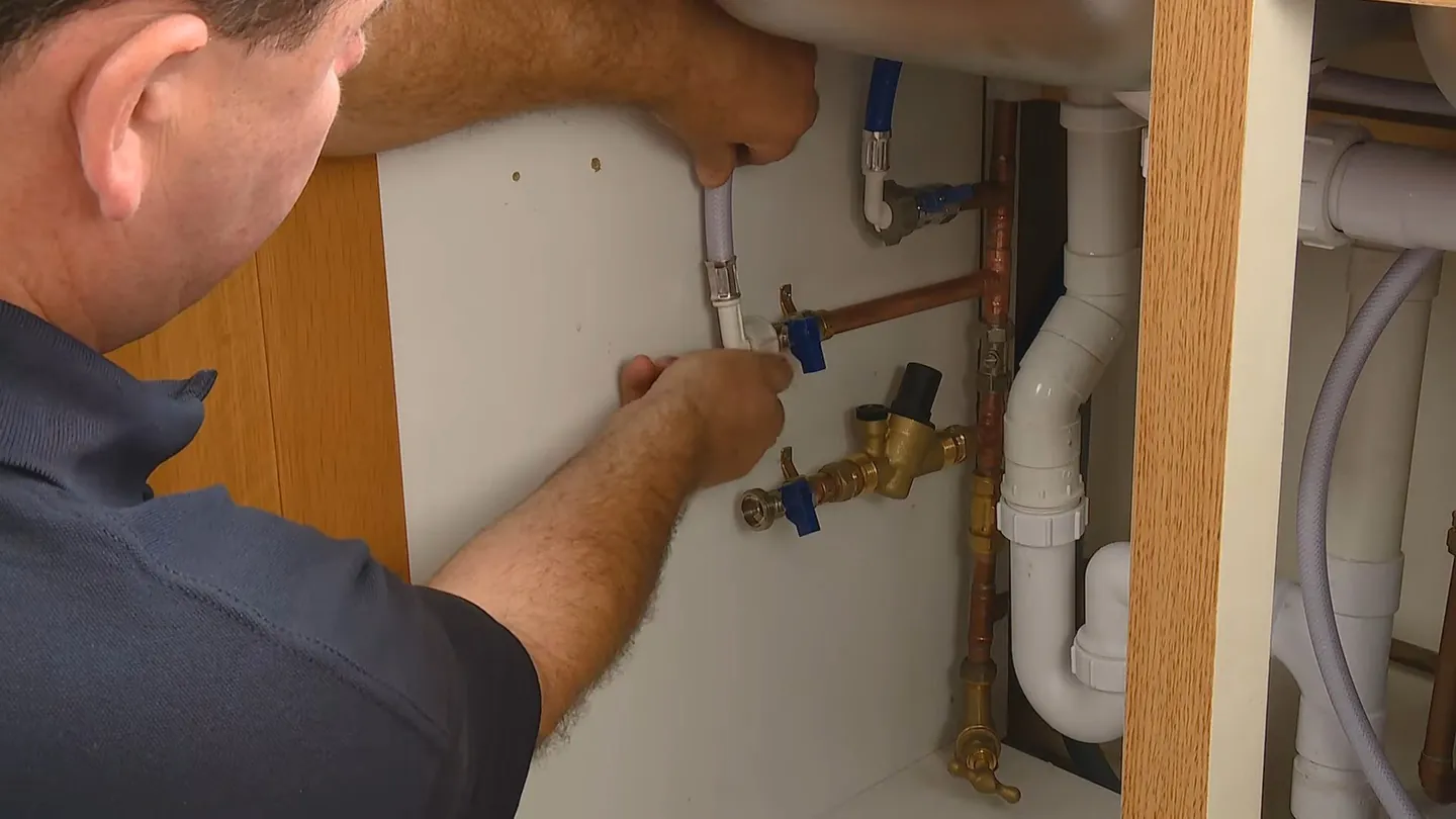 Man reaching under a sink toward angle stop valves and white drain pipes
