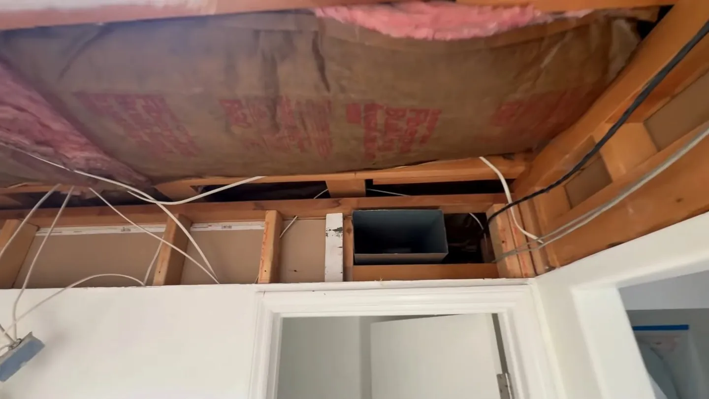 Open ceiling cavity with pink insulation, white lines and a small dark box between joists