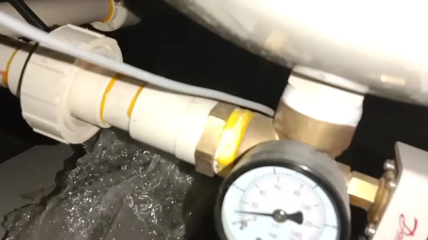Pressure gauge on a brass fitting with white pipe and running water beneath it
