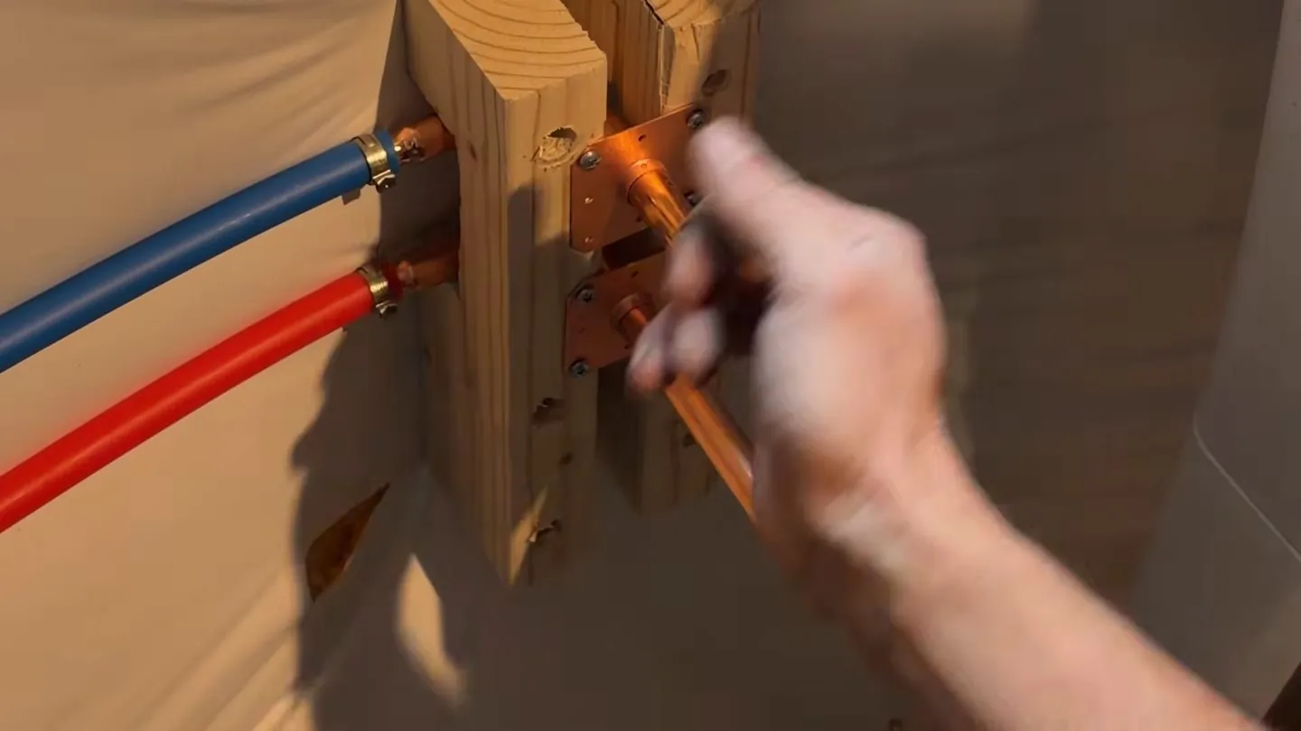 Hand at red and blue PEX stub-outs and a copper stub on a wooden mounting block