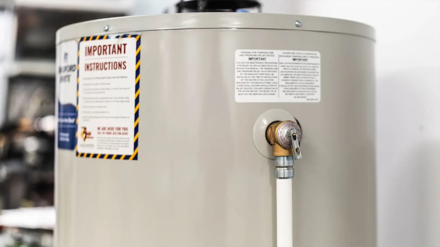 Side of a tank water heater with a relief valve fitted and a white pipe running down from it