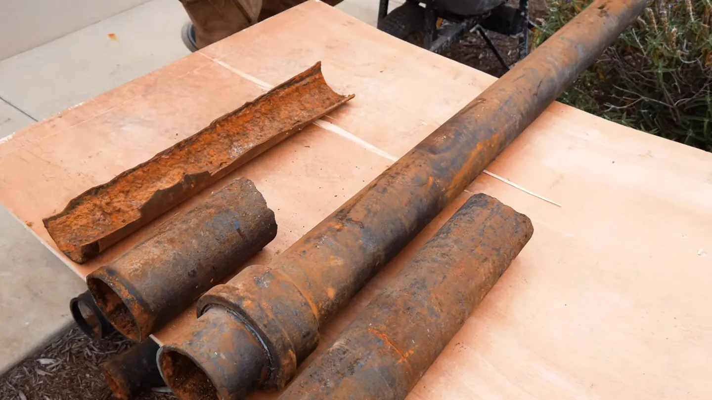 Cut-open and whole sections of rusted iron pipe lying on a sheet of plywood
