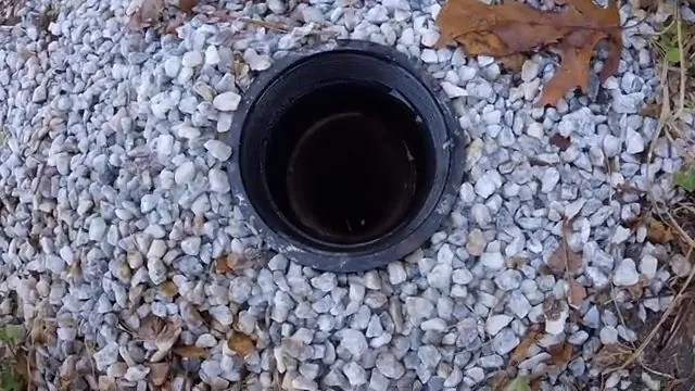 Round black pipe opening with its cap off, set in white landscaping gravel