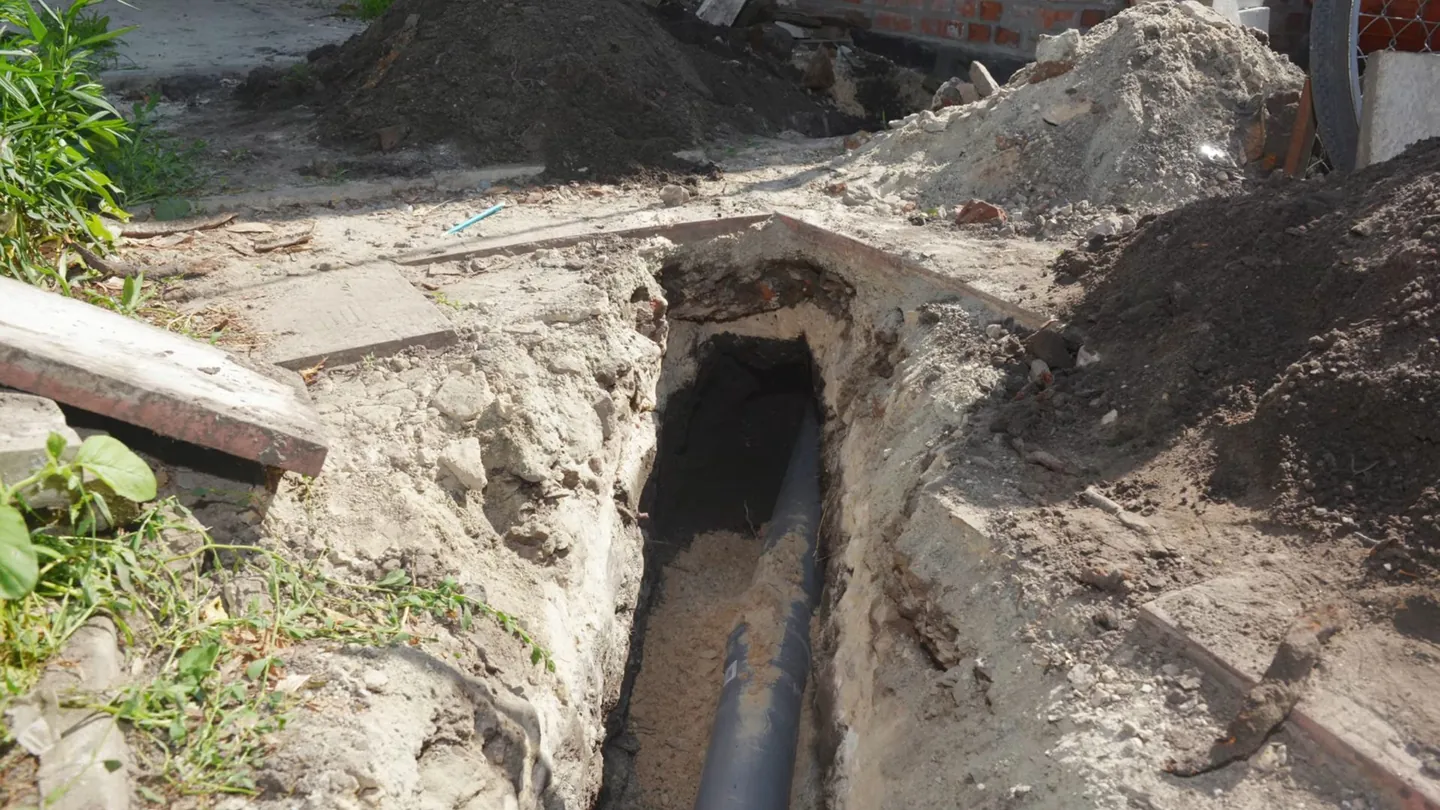 Black pipe lying in a narrow dug trench with sandy soil on both sides