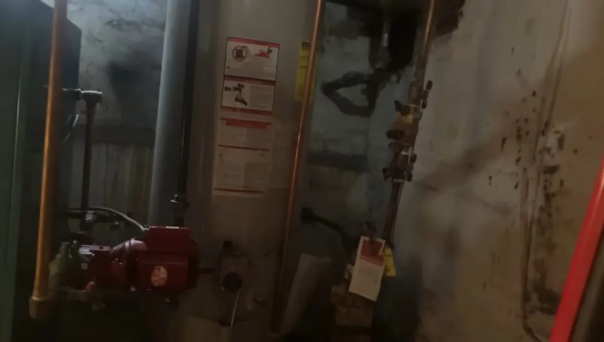 Utility room with a red circulating pump, old iron pipes and valves, and a white tank on the right