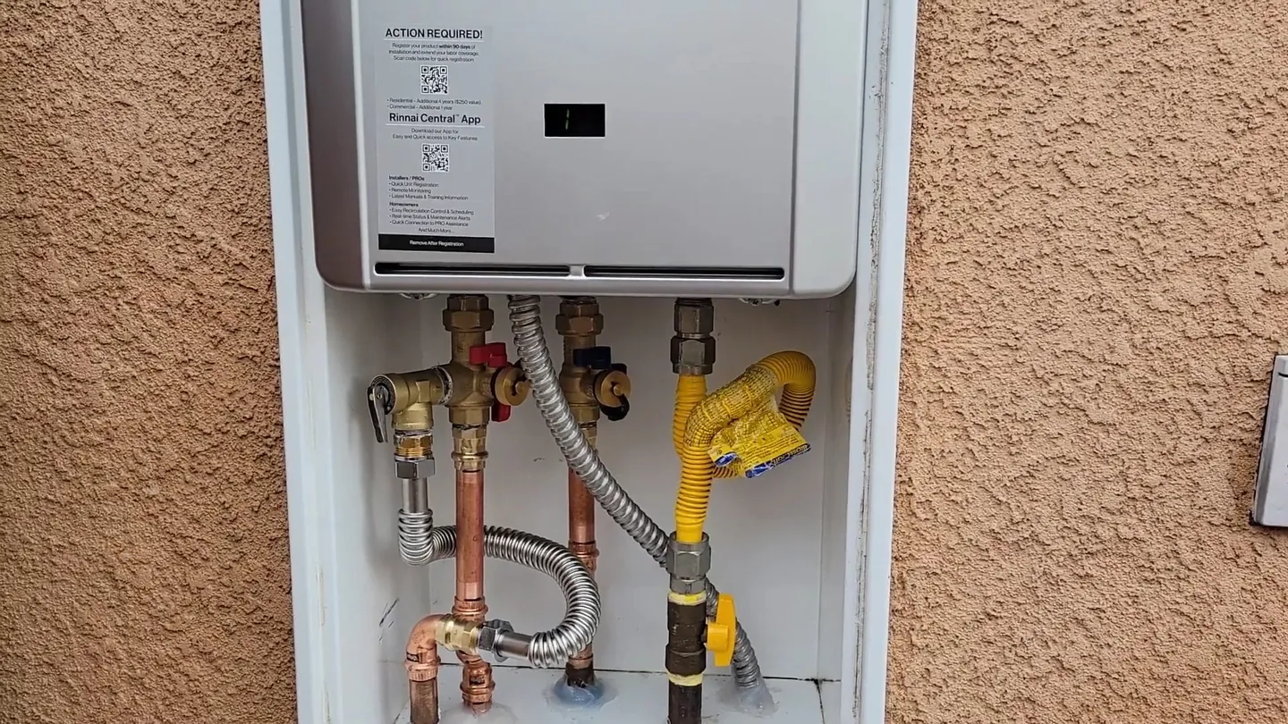 Wall-mounted tankless water heater on a stucco wall with copper and gas connections below it
