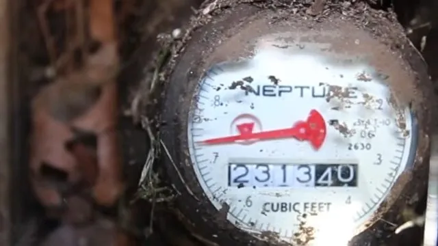 Close view of a water meter dial with a red sweep hand and an odometer-style reading