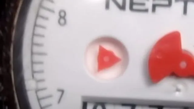 Close view of a water meter face with a red triangle flow indicator and a red sweep hand