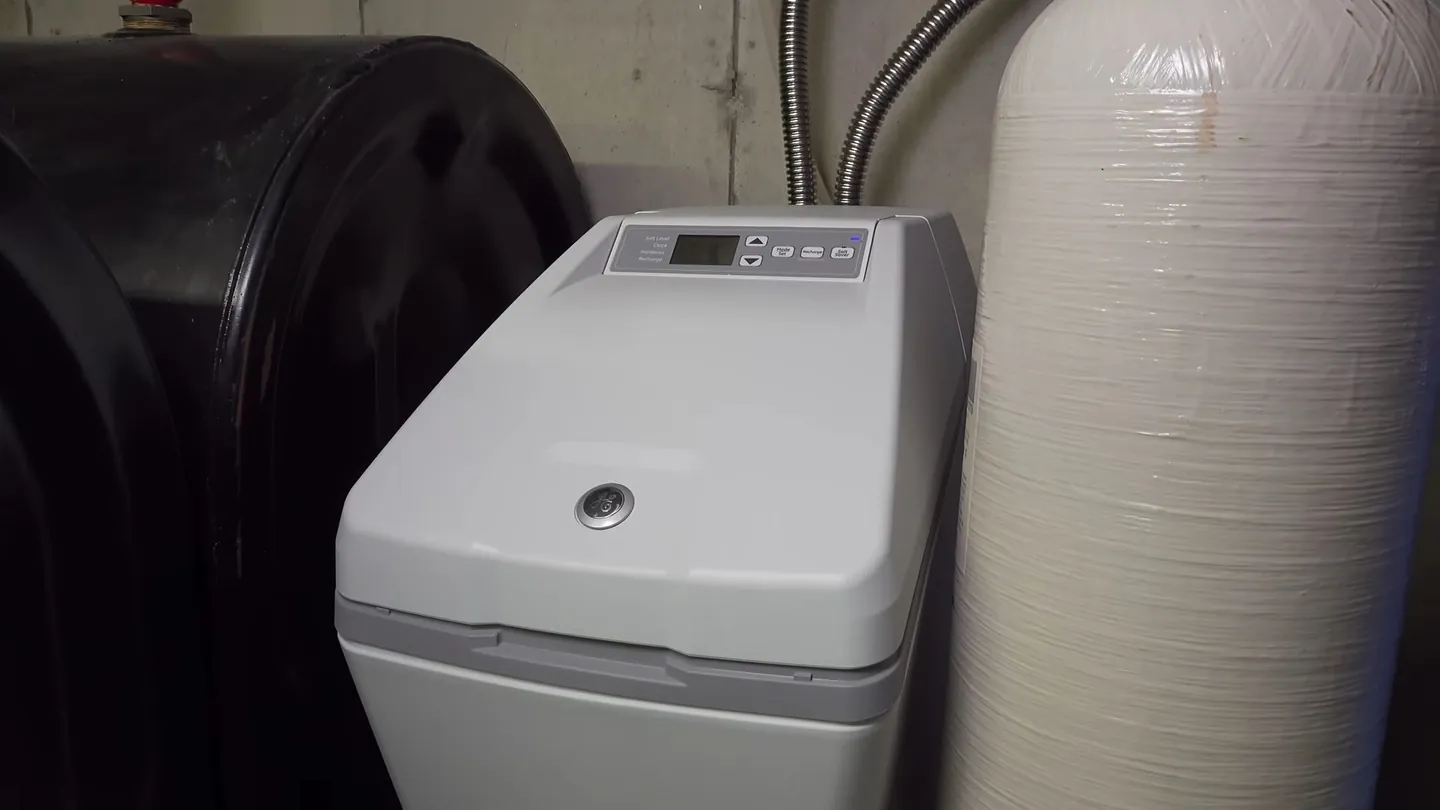 Water softener cabinet beside a large black tank and a tall resin tank against a utility wall