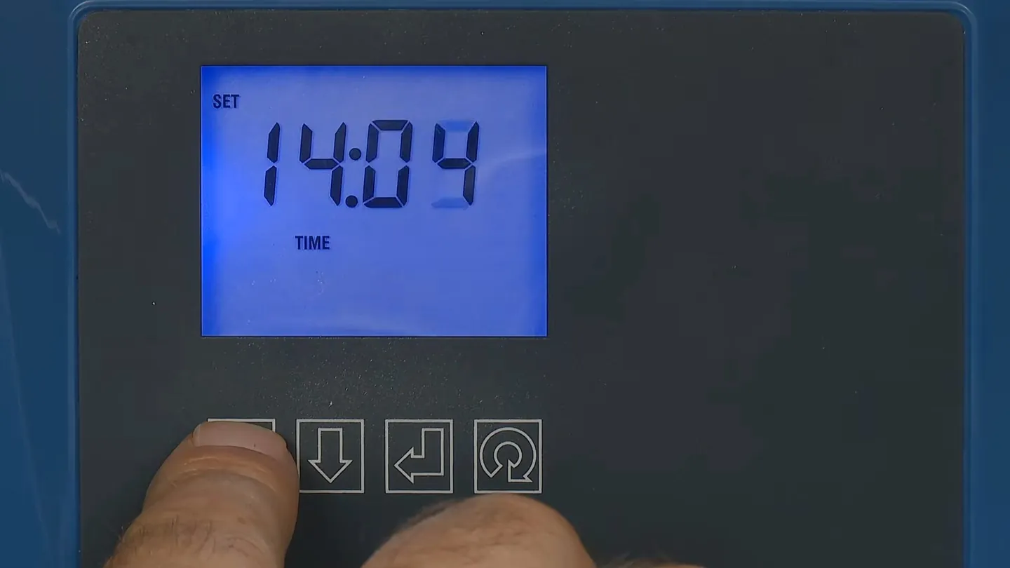 Backlit softener control panel showing a time of day with a finger on the buttons