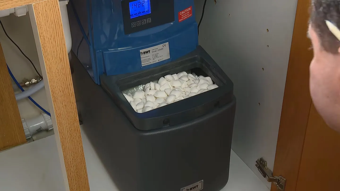 Softener installed in a cupboard with its lid off and salt pellets visible in the tank