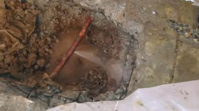 Water spraying from a copper pipe at the bottom of a mud-filled excavation