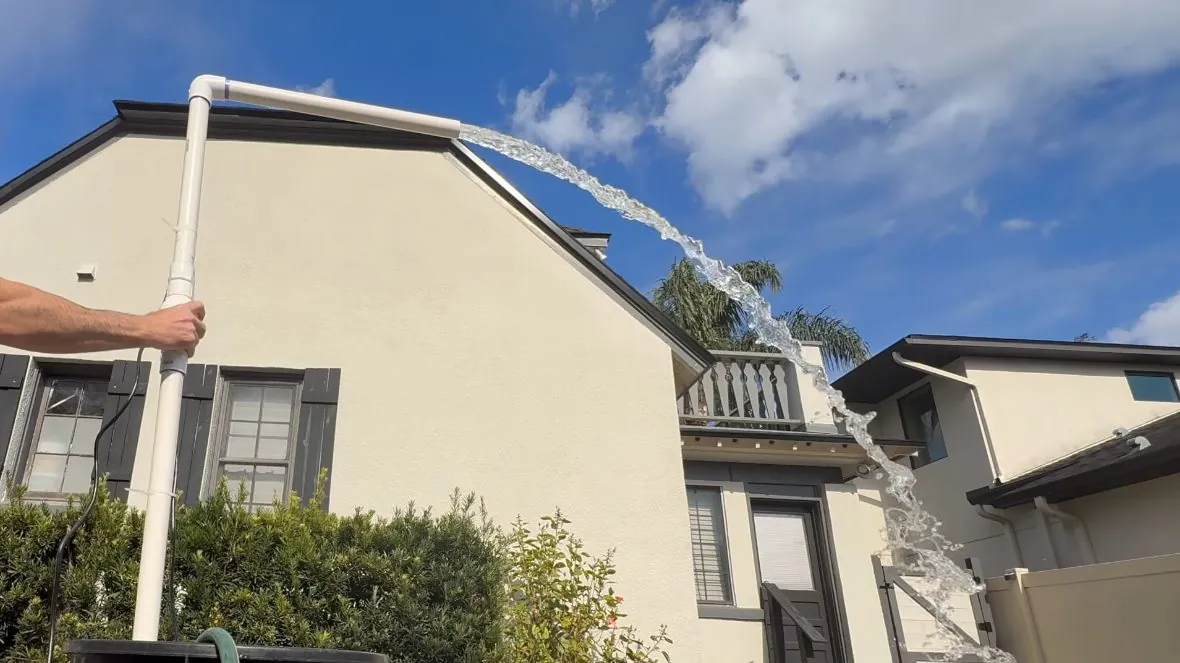 Two-story beige house with water streaming from a white pipe above the roofline