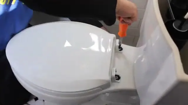 White toilet with a hand using an orange-handled tool at the back of the tank